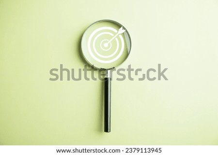 Features a target board captured inside a magnifier glass, illustrating the focus on business objectives, target search concept, and attaining success. Isolated on a background with copy space.