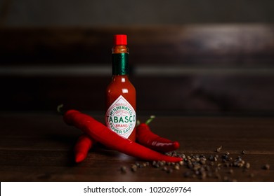 February 06, 2018, Belarus, Minsk. Horizontal photo of a tabasco sauce bottle with red chilli and black peppers, dark wooden background. Selective focus.