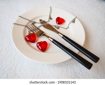 February 14 Is Valentine's Day, A Holiday For All Lovers. Still Life Of A White Plate, Knife, Fork, Three Red Hearts, Two Together, One Lonely. Metal Chains. Symbol Of Love, Adultery And Heartbreaking