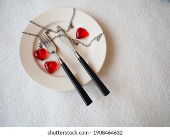 February 14, Valentine's Day, A Holiday For All Lovers. Still Life Of A White Plate, Knife, Fork, Three Red Hearts, Two Together, One Lonely. Metal Chains. Symbol Of Love,  Adultery And Heartbreaking