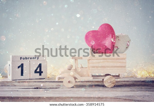 February 14th wooden vintage calendar with wooden\
toy truck with hearts. valentine\'s day celebration concept. vintage\
filtered with glitter\
overlay