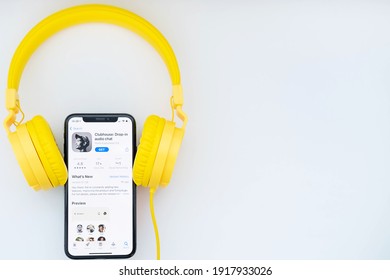 February 16, 2021, Russia, Orenburg: iPhone and yellow headphones on a white background. Clubhouse application on the phone screen. New social network powered by Apple.