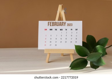 February 2023. Calendar for two thousand twenty-third year on wooden stand. Calendar sheet for whole month is on desktop next to green branch. Concept of the New Year