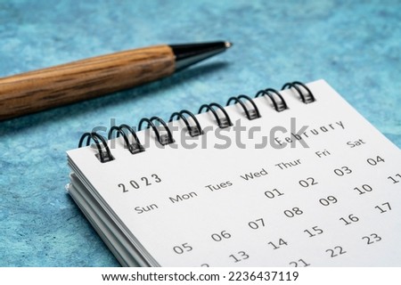 February 2023 - small spiral desktop calendar with a stylish pen  against textured paper,  time and business concept