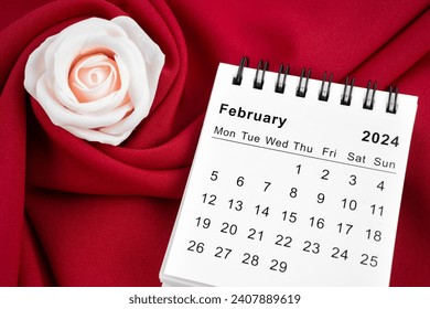 February 2024 desk calendar and pink rose on red textile background.
