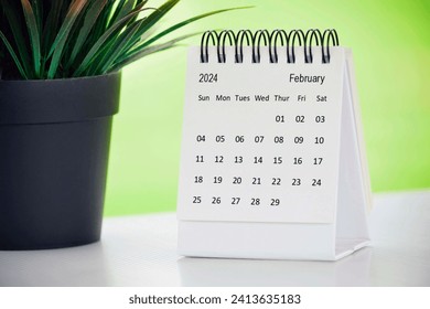 February 2024 desk calendar with potted plant on a desk with green background. Copy space.