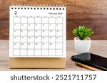 A February 2025 desk calendar on wooden table with black smartphone.