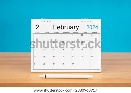 February monthly desk calendar for 2024 year and pen on wooden table with blue color background.