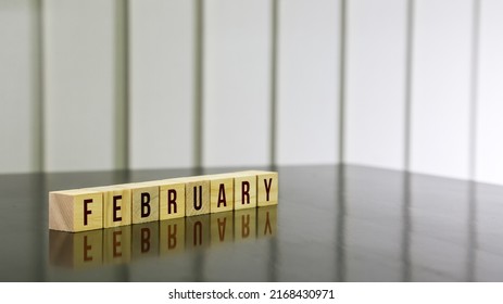 FEBRUARY Word On Wooden Cube On Black Gloss Wooden Table. Selected Focus