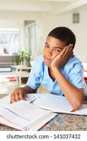 Fed Up Boy Doing Homework In Kitchen