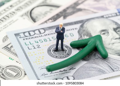 FED consider interest rate hike, world economics and inflation control, miniature businessman leader standing on US Federal Reserve emblem on dollars banknote with green arrow rising up.