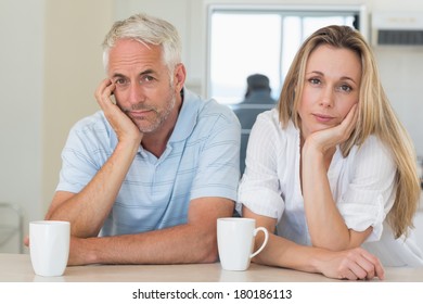 Fed Up Couple Sitting At The Counter At Home In The Kitchen