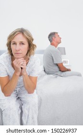 Fed Up Couple Sitting On Different Sides Of Bed Having A Dispute With Woman Looking At Camera In Bedroom At Home