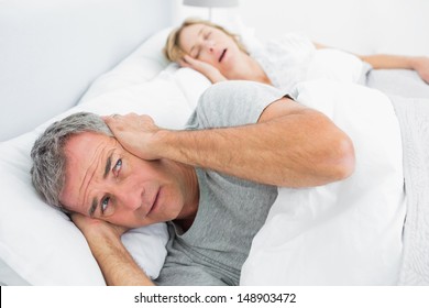 Fed Up Man Blocking His Ears From Noise Of Wife Snoring At Home In Bedroom