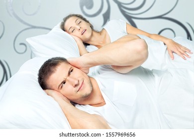 Fed Up Man Blocking His Ears From Noise Of Wife Snoring At Home In Bedroom