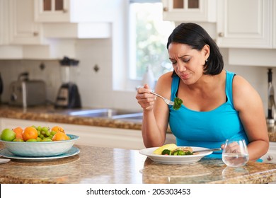 Fed Up Overweight Woman Eating Healthy Meal In Kitchen