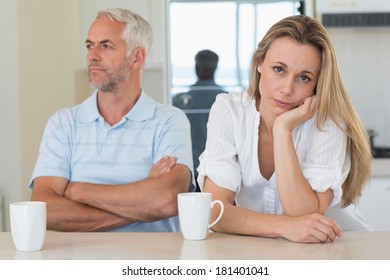 Fed Up Woman Sitting At The Counter With Her Partner At Home In The Kitchen