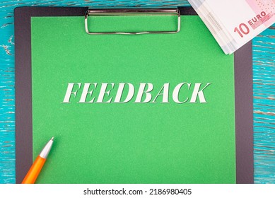 FEEDBACK - word (text) and a bundle of money, euro bills on a green background of a notebook, a pen and a wooden table. Business concept: buy, sell, commerce (copy space).