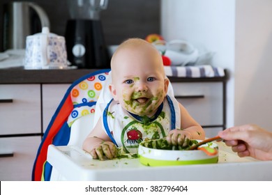 Feeding. Adorable Baby Child Eating With A Spoon In High Chair. Baby's First Solid Food