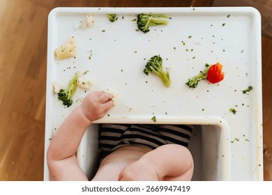 Feeding. Baby's first solid food. Baby boy eating vegetables. Child eating broccoli at home. Smiling beautiful baby curiously trying different vegetables.