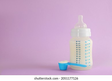 Feeding Bottle With Infant Formula And Scoop Of Powder On Lilac Background, Space For Text. Baby Milk