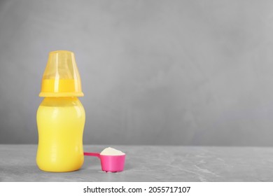 Feeding Bottle With Infant Formula And Scoop Of Powder On Grey Table, Space For Text. Baby Milk