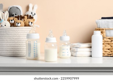 Feeding bottles with milk and other baby accessories on white table near beige wall