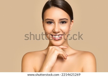  Feel so clean and fresh. Beautiful brunette model portrait with shiny healthy skin and theeth touching her chin, isolated on beige background
