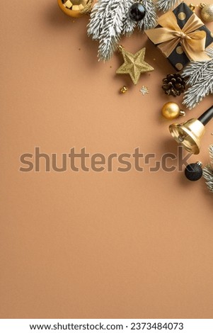 Feel holiday magic with this festive Christmas scene. Overhead vertical shot of elegant giftbox, golden and black baubles, gleaming confetti, jingling bell, frosted fir branches on terracotta backdrop