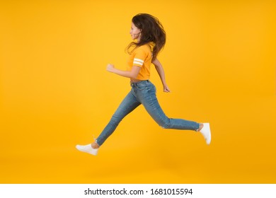 Feel Inner Energy. Pretty Girl With Long Hair. Fashion Style. Beauty And Make Up. Energetic Woman Running Or Jumping. Skinny Jeans Suits Her. Sexy Girl Yellow Background. Sensual Girl In Casual Style.