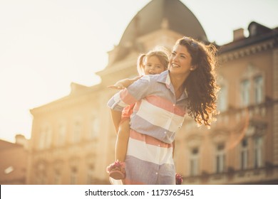 I Feel Safe On Your Back. Mother And Her Daughter Playing Together On City Street. Close Up. Copy Space.