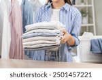 Feel softness, chore of pretty asian young woman hand holding pile clothing from table, stack folding clean clothes after washing, laundry and dry. Household working at home. Laundry of maid concept.