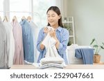 Feel softness, hygiene. Smile asian young woman touching fluffy white shirt smelling fresh clean clothes, pretty girl comfort sniff after washing laundry. Household work at home, chore of maid concept