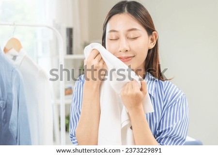Feel softness, hygiene. Smile asian young woman touching fluffy white shirt smelling fresh clean clothes, pretty girl comfort sniff after washing laundry. Household work at home, chore of maid concept