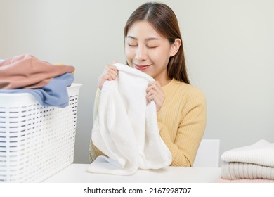 Feel Softness, Smiling Asian Young Woman, Girl Touching Fluffy Towel Cotton, Smelling Fresh Clean Clothes On Table After Washing, Laundry, Dry. Household Working At Home. Laundry And Maid.