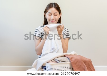 Feel softness, smiling asian young woman, girl touching fluffy towel cotton, smelling fresh clean clothes on table after washing, laundry, dry. Household working at home. Laundry and maid.