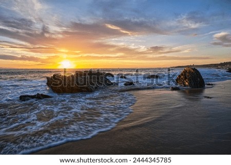 Feel the tranquility as the sun gently sets over the picturesque beach, casting a warm, golden glow over the rugged rocks and calm waters. A perfect moment of serenity captured in nature's beauty.