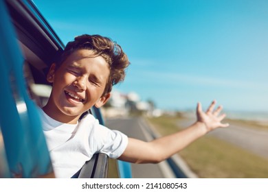 Feel The Wind In Hair - And Face. Shot Of A Happy Young Boy Leaning Out Of The Car Window On A Trip To The Beach.