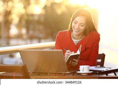 Feelance working with laptop in winter taking notes in an agenda outdoors - Powered by Shutterstock