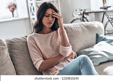 Feeling bad. Frustrated young woman suffering from the headache while sitting on the sofa at home    