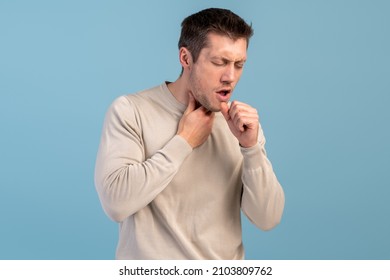 Feeling bad. Young caucasian man suffers pain in throat and coughing due a virus or infection while standing isolated over blue wall. Stock photo  - Shutterstock ID 2103809762