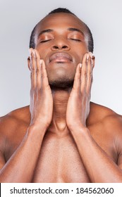 Feeling Clean And Fresh. Young Shirtless African Man Touching His Face With Hands And Keeping Eyes Closed While Standing Against Grey Background