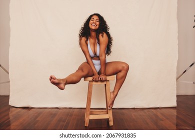 Feeling comfortable in blue underwear. Happy young woman embracing her natural body while sitting alone against a studio background. Body positive young woman smiling cheerfully in a studio.