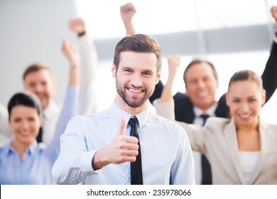 Feeling confident in his team. Happy businessman showing his thumb up and smiling while his colleagues standing in the background 