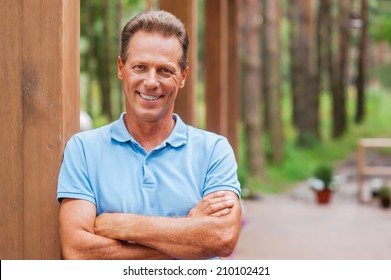 Feeling Confident And Relaxed. Confident Mature Man Keeping Arms Crossed And Smiling While Standing Outdoors 