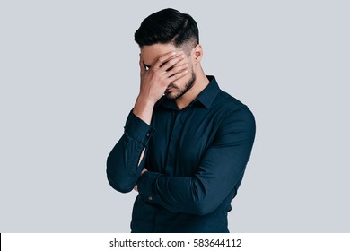 Feeling Depressed.  Exhausted Young Man Covering Face With Hand While Standing Against Grey Background