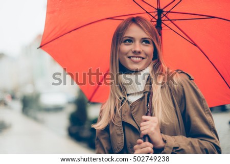 Feeling dry and protected. Attractive young woman carrying umbrella and smiling while standing on the street 