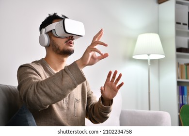 Feeling excited and amazed. Young Asian man wearing VR goggles while playing video games with hands reaching out to touch something in virtual world.