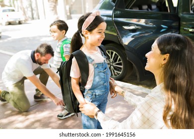 Feeling Excited For School. Pretty Young Girl Smiling To Her Beautiful Mom After Getting Out Of The Car To Go To School With Her Little Brother