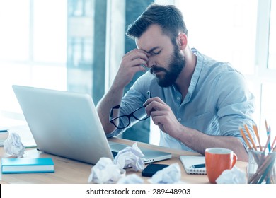 Feeling exhausted. Frustrated young beard man massaging his nose and keeping eyes closed while sitting at his working place in office 